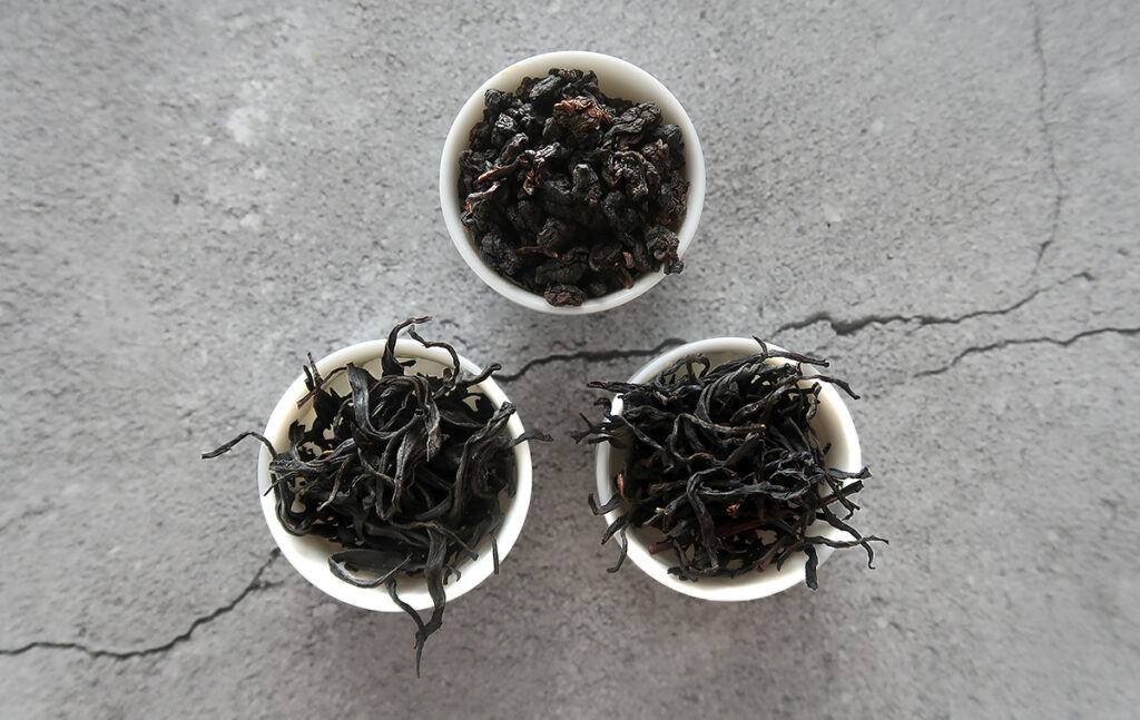 Close-up of three Taiwanese oolong teas – Red Charm, Red Ruby, and High Mountain – showing distinct leaf shapes and colors, highlighting Taiwan's premium black and oolong tea varieties.